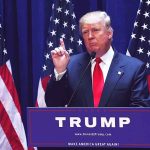 Person speaking at podium with multiple American flags