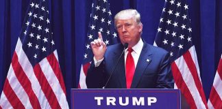 Person speaking at podium with multiple American flags