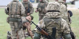 Soldiers in camouflage gear gathered on grass field