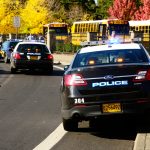 Police cars and school buses on roadside with cones