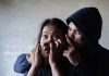 Man holding womans mouth gesturing silence