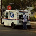 USPS mail carrier at truck near stop sign