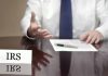 IRS official gesturing v with documents and pen