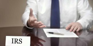 IRS official gesturing v with documents and pen