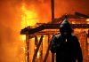 Hooded figure standing before a burning building