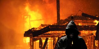 Hooded figure standing before a burning building