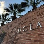 Brick wall with "UCLA" lettering and palm trees.
