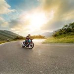 Person rides motorcycle on curved mountain road at sunset