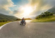 Person rides motorcycle on curved mountain road at sunset