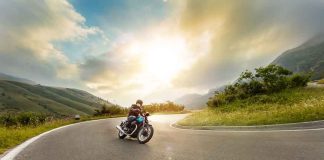 Person rides motorcycle on curved mountain road at sunset