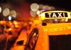 Close-up of a taxi sign illuminated at night with blurred city lights in the background