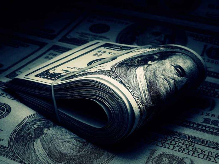 shutterstock_125542373.jpg A rolled stack of hundred-dollar bills on a background of more banknotes