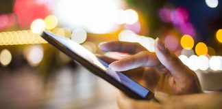 A person's hand using a smartphone in a city at night with blurred lights in the background
