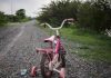 Pink children's bike with training wheels on gravel path
