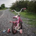 Pink children's bike with training wheels on gravel path