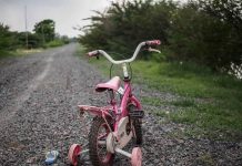 Pink children's bike with training wheels on gravel path