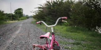 Pink children's bike with training wheels on gravel path