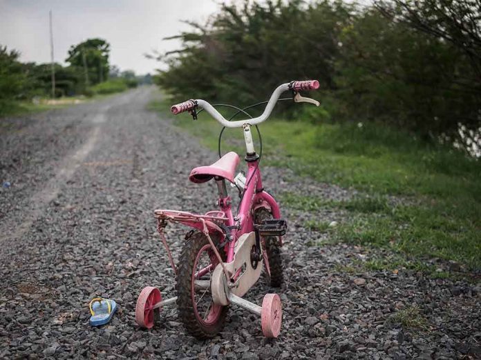 Pink children's bike with training wheels on gravel path