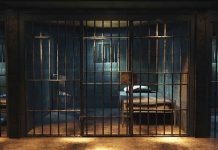 Empty prison cell with metal bars and bed