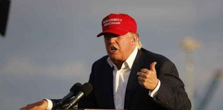 Person speaking at a podium wearing a red hat