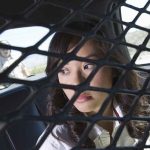 A woman sitting in the back of a police car, looking through a protective mesh barrier