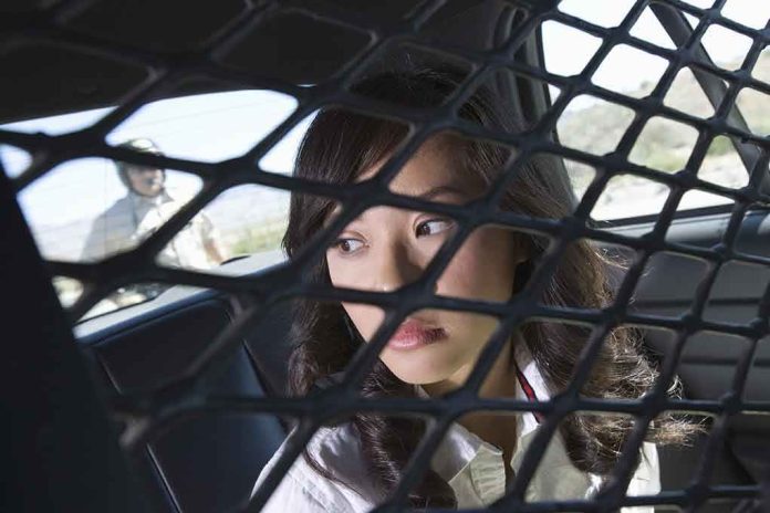 shutterstock_110787518.jpg A woman sitting in the back of a police car, looking through a protective mesh barrier