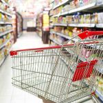 A shopping cart in a grocery store aisle filled with colorful products