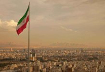 Iranian flag waving over a city skyline with mountains in the background