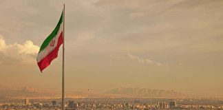 Iranian flag waving over a city skyline with mountains in the background