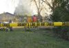 Yellow police tape marking a restricted area at a fire scene with firefighters in the background