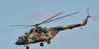 Camouflage military helicopter in flight against blue sky.