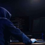 Hooded figure using dual monitors in dark room