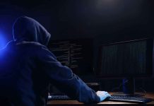 Hooded figure using dual monitors in dark room