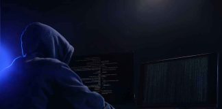 Hooded figure using dual monitors in dark room