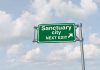 Two Patriots Dead: Sanctuary Policies Under Siege Green road sign saying sanctuary city next exit