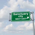 Two Patriots Dead: Sanctuary Policies Under Siege Green road sign saying sanctuary city next exit