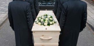 Four people carrying a coffin with white flowers