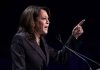 Person speaking at podium with raised finger