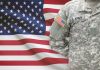 Trump’s Military Move: Overreach or Necessity? Soldier in camouflage uniform standing before American flag