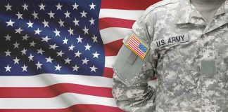 Soldier in camouflage uniform standing before American flag