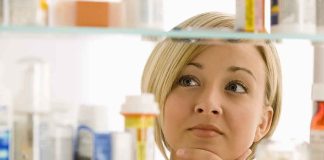 A woman thoughtfully looking at a medicine cabinet filled with various medications
