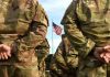 Soldiers stand in formation with American flag in background.