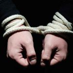 Hands tied with rope in the dark.