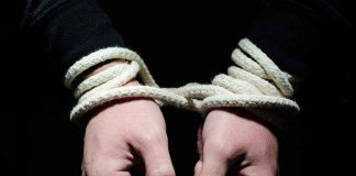 Hands tied with rope in the dark.