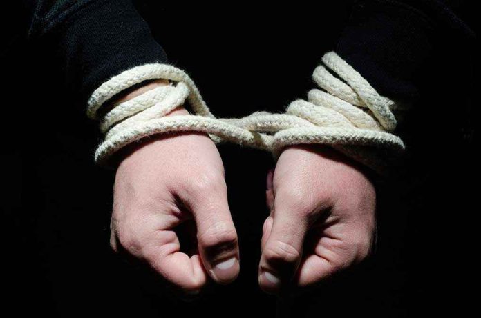 155804528 Hands tied with rope in the dark.