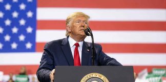 Man speaks at podium with U.S. flag background.