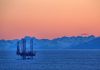 An oil rig in the ocean with a backdrop of mountains during sunset