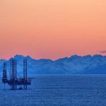 Global Oil Prices SPIKE – What’s Next? An oil rig in the ocean with a backdrop of mountains during sunset