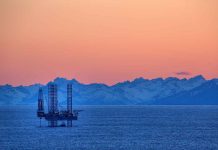 An oil rig in the ocean with a backdrop of mountains during sunset