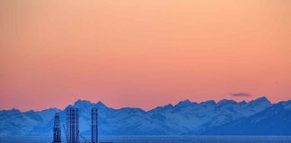 An oil rig in the ocean with a backdrop of mountains during sunset